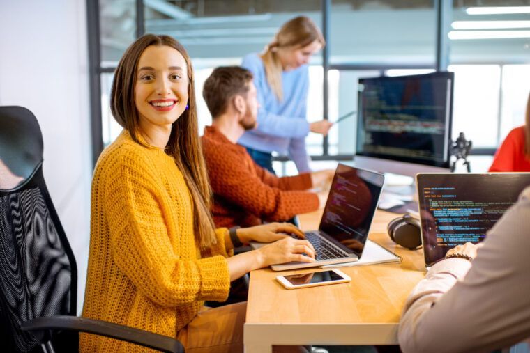 Programistka przy komputerze w biurze, w tle zespół
